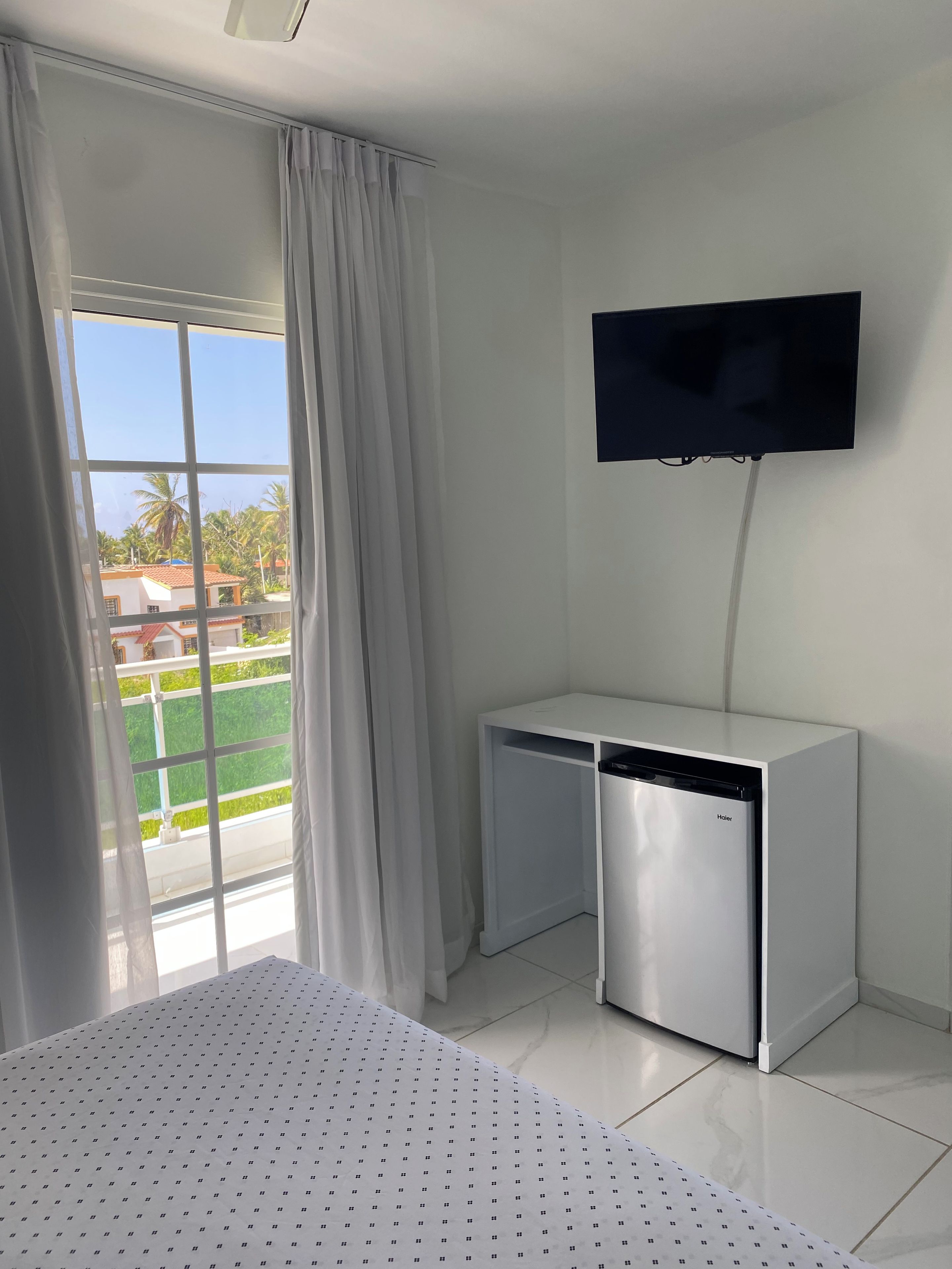 Habitación de hotel con cama, televisión en la pared y ventana con cortinas.