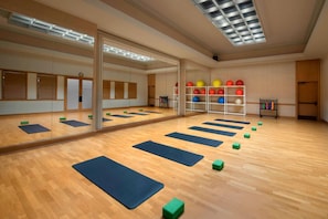 A spacious room with wooden flooring, exercise mats, and a mirrored wall.