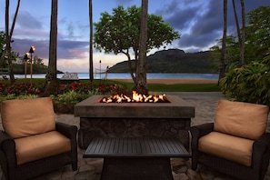 A fire pit with two wicker chairs, a view of the beach, and a cloudy sky.