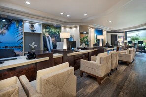 A hotel reception area with a desk, chairs, and a mural of a beach scene.
