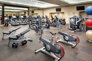 Ein Fitnessstudio mit verschiedenen Trainingsgeräten, darunter Laufbänder, Crosstrainer und Kraftgeräte.