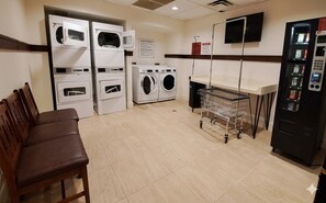 A laundry room with stacked washers and dryers, a vending machine, and a seating area.