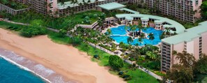 Ein Resort mit großem Pool, umgeben von Palmen und einem Strand.