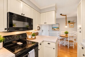 Een keuken met witte kasten, een zwart fornuis, en een eethoek met een houten tafel en stoelen.