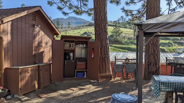 A rustic cabin with a small kitchen area, a dining table, and a barbecue grill.