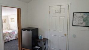 A room with a bed, a refrigerator, a small table with items, and a door with a map on the wall.