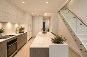 Une cuisine moderne dotée d’un îlot central, d’appareils électroménagers intégrés et d’un escalier en verre.