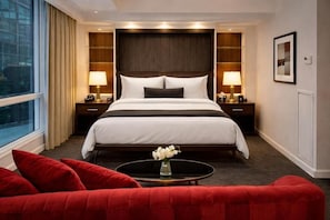 A hotel room with a large bed, two bedside tables with lamps, a red sofa, a small round table with a vase, and a window with curtains. - Nova The Entertainment District Toronto (Toronto)