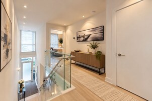 A modern interior with a glass staircase, a wooden console, and a framed artwork on the wall.