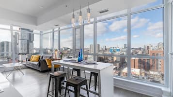 A modern kitchen with a large island, bar stools, and a city view through expansive windows.