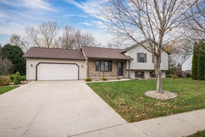 A two-story house with a garage, a front yard with a tree, and a clear sky. - Your Home Away From Home! Only 20-25 Minutes to Madison! (Stoughton)