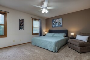 A bedroom with a bed, a nightstand, a chair, a ceiling fan, a window with blinds, and a painting on the wall. - Your Home Away From Home! Only 20-25 Minutes to Madison! (Stoughton)