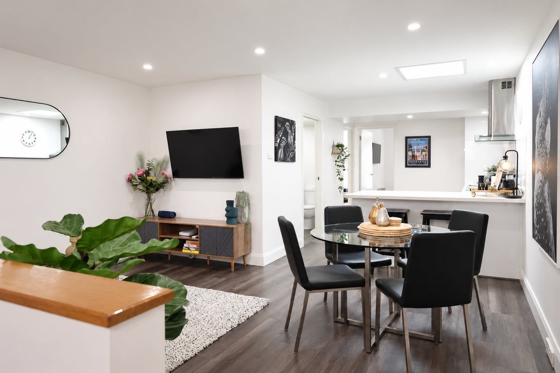 Ein modernes Wohnzimmer mit Essbereich, einem an der Wand befestigten Flachbildfernseher und einer im Hintergrund sichtbaren Küche.