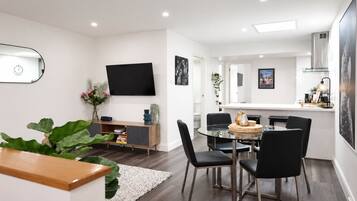 Ein modernes Wohnzimmer mit Essbereich, einem an der Wand befestigten Flachbildfernseher und einer im Hintergrund sichtbaren Küche.