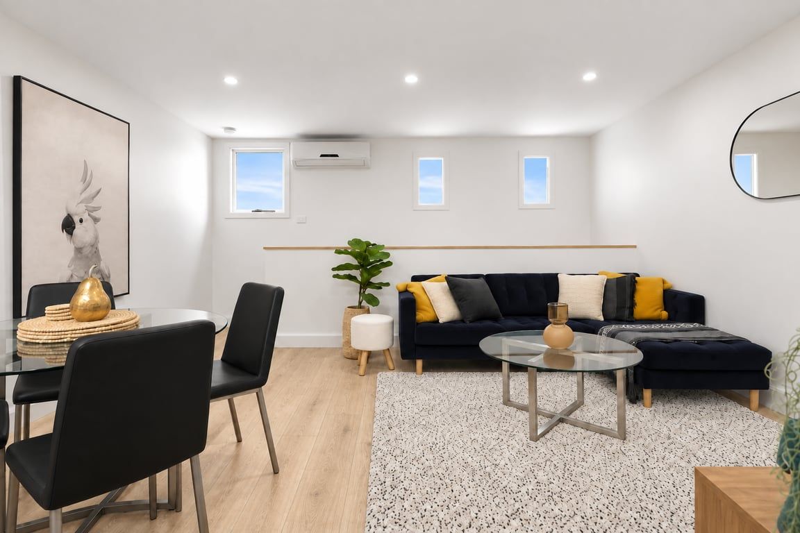 Una sala de estar moderna con un sofá negro, una mesa de centro de vidrio y un comedor con una mesa y sillas de vidrio.