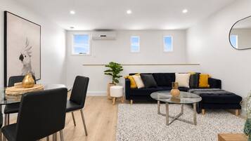 Una sala de estar moderna con un sofá negro, una mesa de centro de vidrio y un comedor con una mesa y sillas de vidrio.