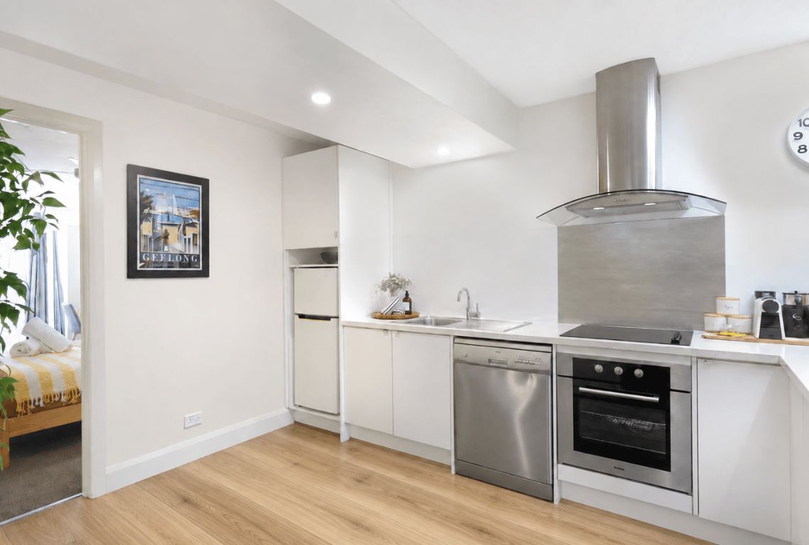 A modern kitchen with white cabinetry, stainless steel appliances, and a wooden floor.