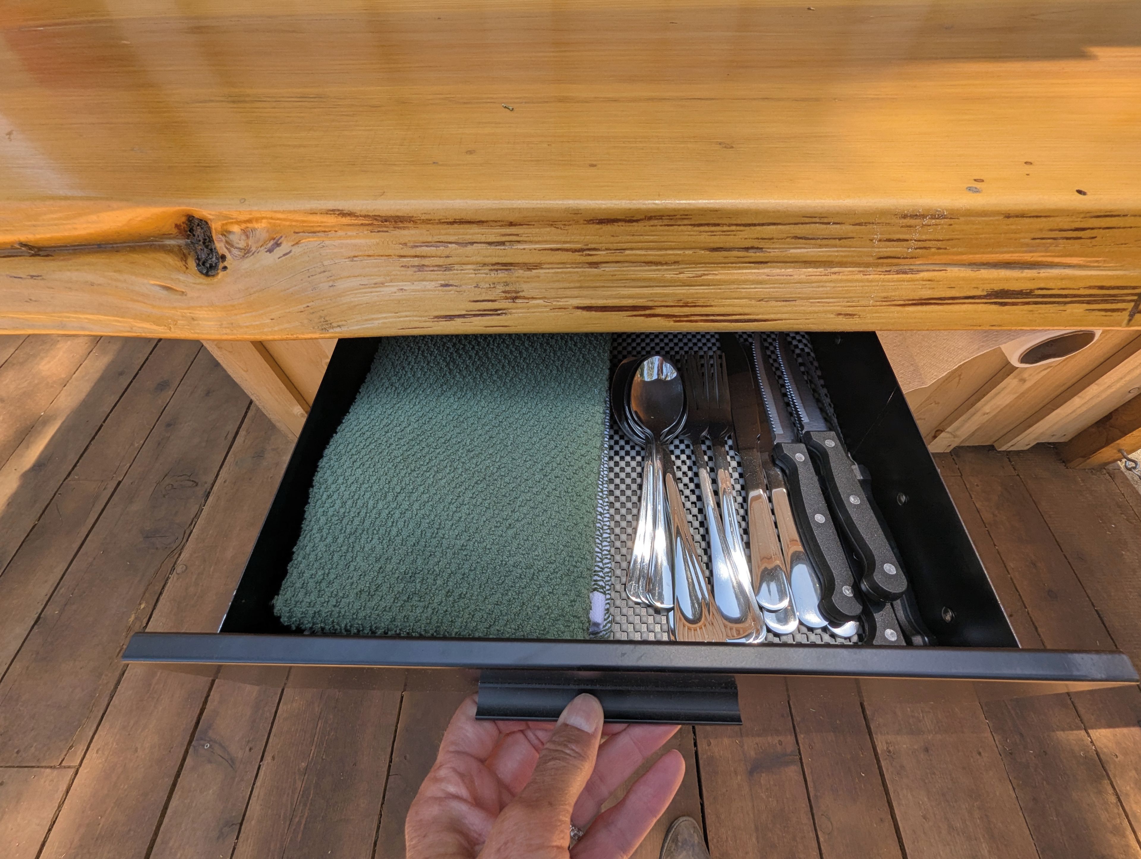 A drawer with a green mat, containing a spoon, fork, knife, and a black-handled knife.