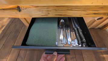 A drawer with a green mat, containing a spoon, fork, knife, and a black-handled knife.