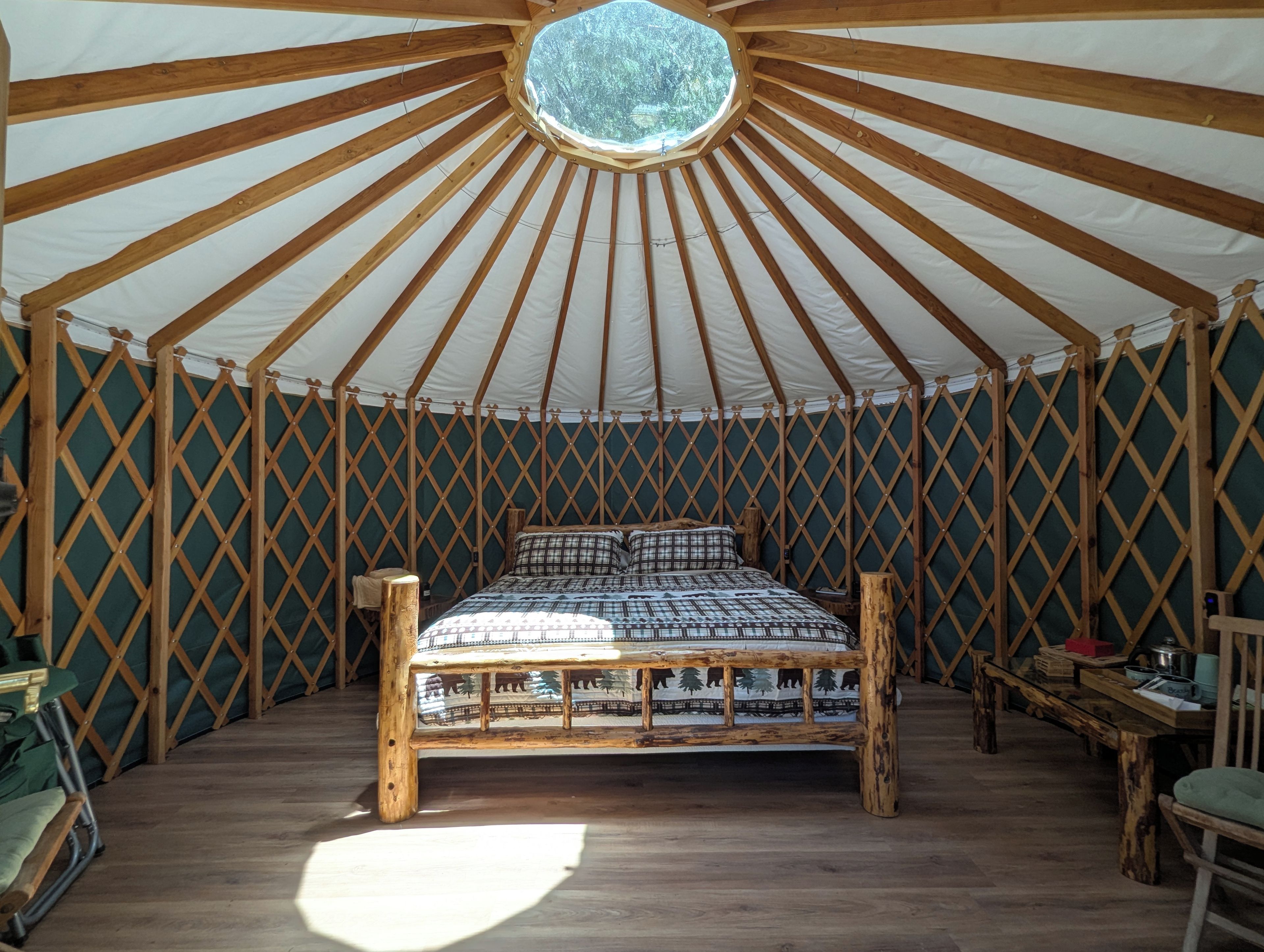 A yurt with a wooden bed, a circular skylight, and a lattice wall.
