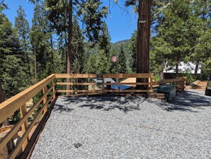 A wooden deck with a gravel path, surrounded by tall trees and a clear sky. - Big Woods Retreat (Miramonte)