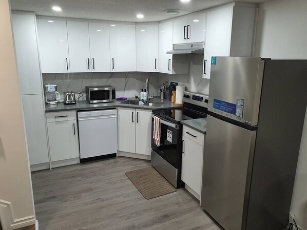 A modern kitchen with white cabinets, stainless steel appliances, and a black countertop. - Beautiful Tranquil 1bedroom Basement Suite (Beaumont)