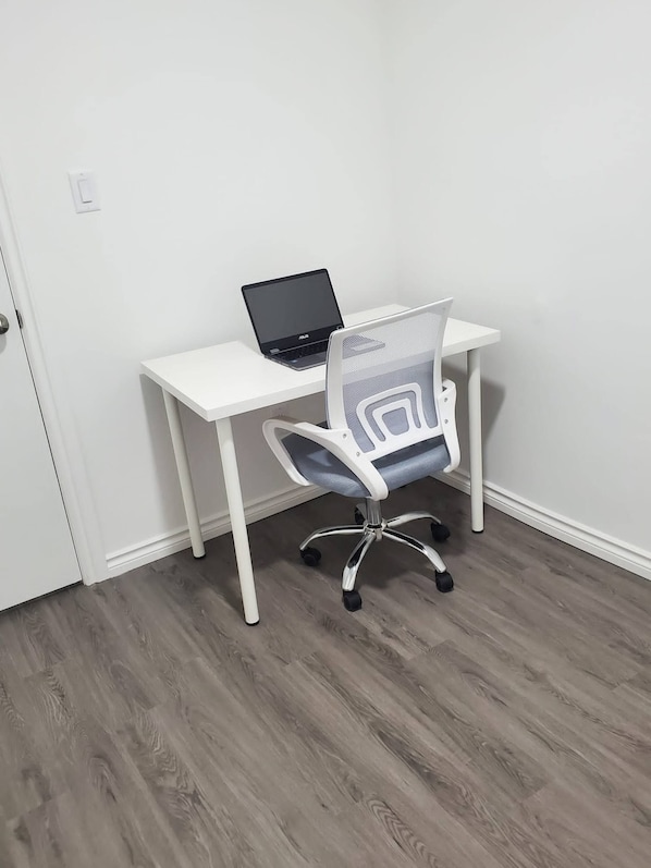 A white desk with a laptop and an office chair in a room with wooden flooring and white walls.