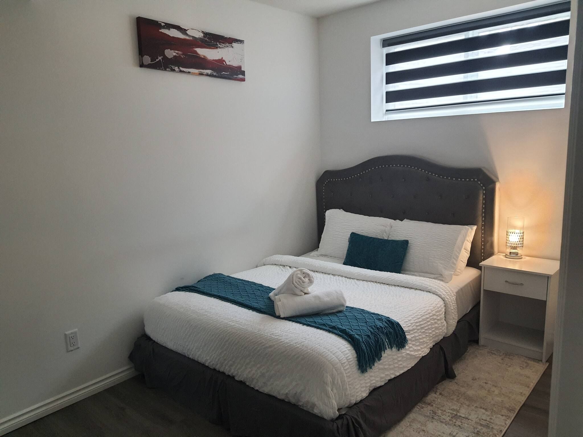 A neatly made bed with a white and teal blanket, a dark headboard, and a bedside lamp.