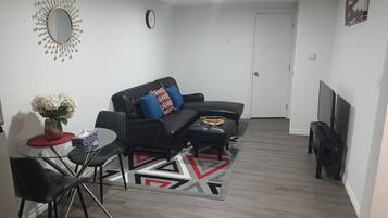 Una sala de estar moderna con un sofá de cuero negro, una mesa de centro de vidrio y una alfombra estampada en rojo y blanco.