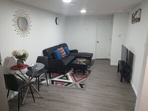 Una sala de estar moderna con un sofá de cuero negro, una mesa de centro de vidrio y una alfombra estampada en rojo y blanco.