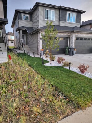 A residential house with a well-maintained lawn, a small tree, and a garage. - Beautiful Tranquil 1bedroom Basement Suite (Beaumont)