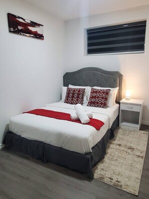 A neatly arranged bedroom with a bed, pillows, a bedside table, and a wall-mounted artwork. - Beautiful Tranquil 1bedroom Basement Suite (Beaumont)