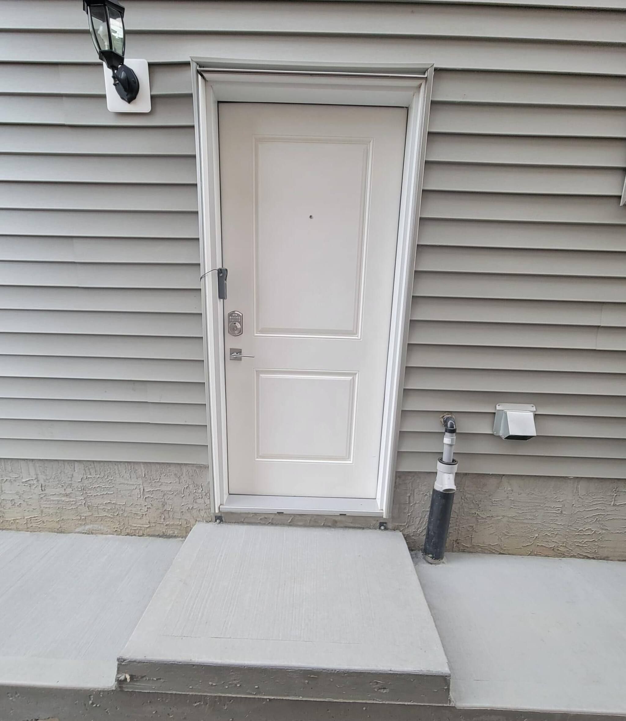 Una puerta principal con un escalón pequeño que lleva a ella, un buzón y una cámara de seguridad montada en la pared.