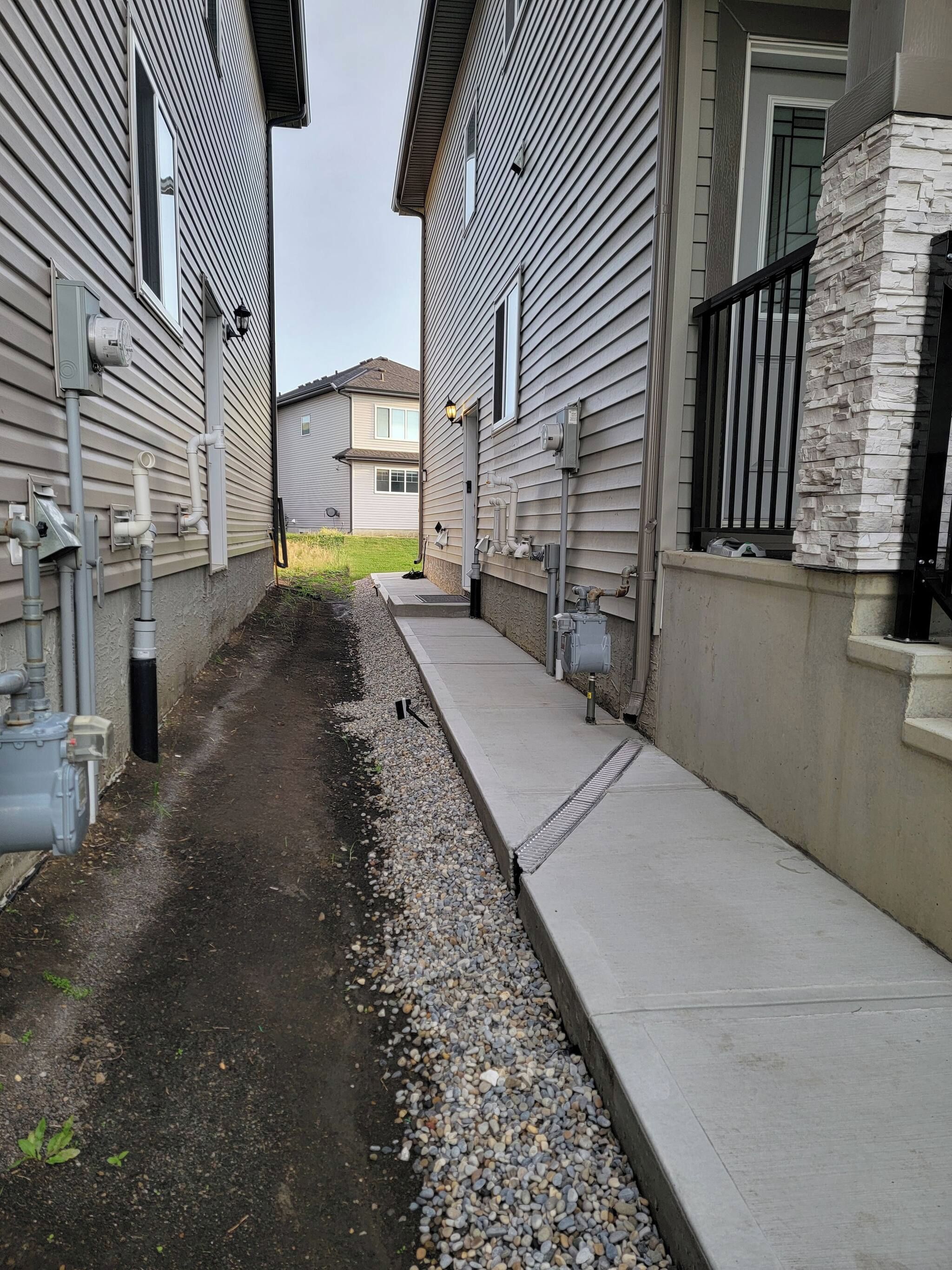 A narrow alleyway between two buildings with visible utility pipes and a concrete pathway.