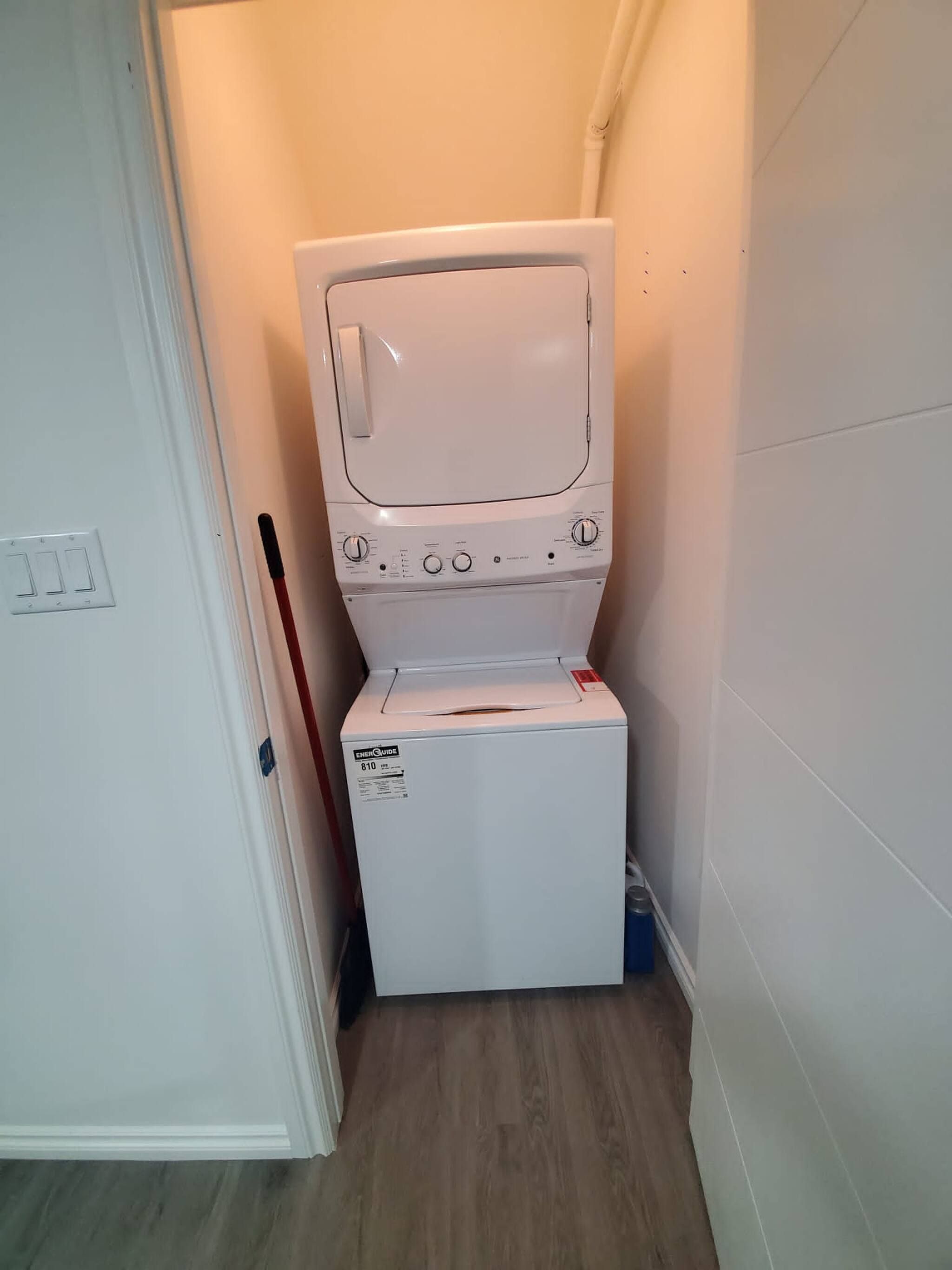 Una unidad compacta de lavadora y secadora en un pasillo estrecho con suelo de madera.