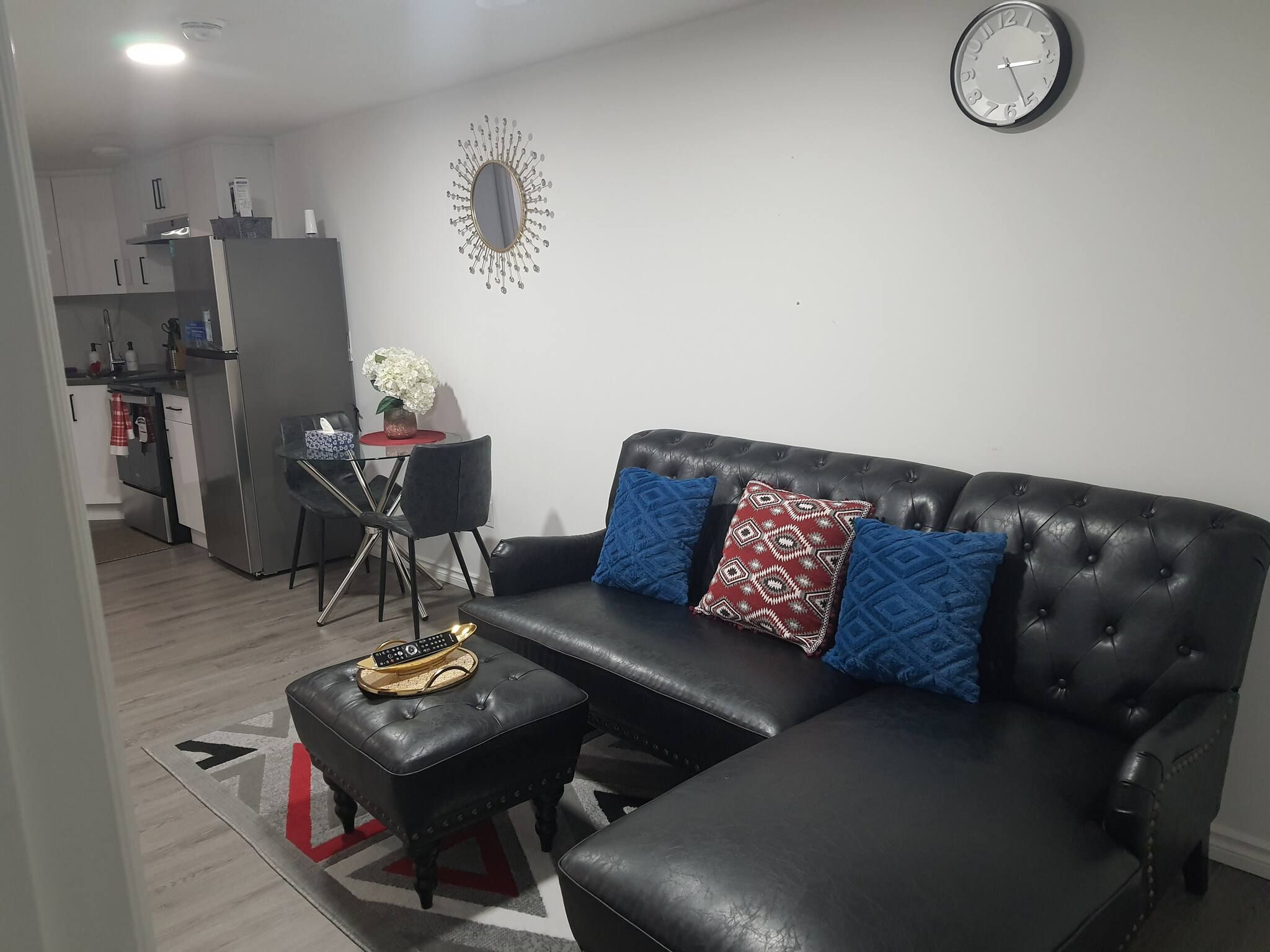 Un salon avec un canapé en cuir noir, une table basse et une horloge murale.