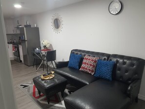 A living room with a black leather sofa, a coffee table, and a wall clock. - Beautiful Tranquil 1bedroom Basement Suite (Beaumont)