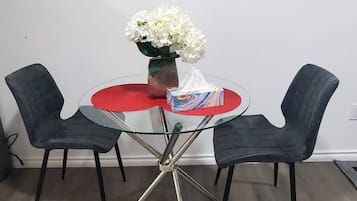 Un comedor con una mesa redonda, dos sillas, un florero con flores y un espejo en la pared.