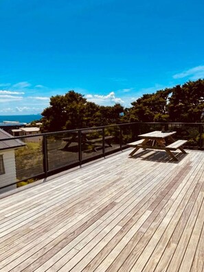 A wooden deck with picnic tables, overlooking a residential area and the sea. - Blue Moon Coastal Escape (Langs Beach)