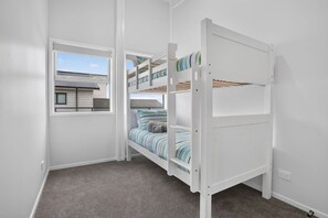 A bunk bed room with a window, carpeted floor, and white walls. - Blue Moon Coastal Escape (Langs Beach)