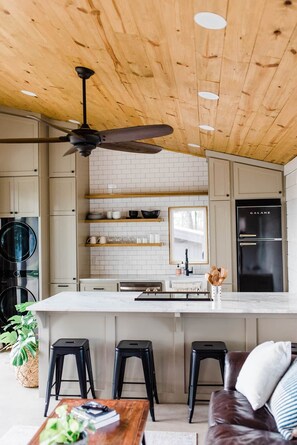 A modern kitchen with a wooden ceiling, a central island with stools, and a refrigerator. - Texas Tiny Cabins #1 - Cozy Getaway Near Texoma (Grayson County)