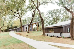 A modern building with a covered patio area, surrounded by trees and a paved walkway. - Texas Tiny Cabins #1 - Cozy Getaway Near Texoma (Grayson County)
