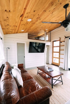 Een woonkamer met een houten plafond, een leren bank, een salontafel en een flatscreen televisie aan de muur.