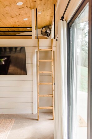 A room with a wooden ladder, a large window, and a ceiling fan. - Texas Tiny Cabins #1 - Cozy Getaway Near Texoma (Grayson County)