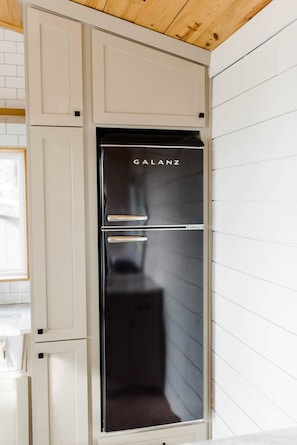 A modern kitchen with a built-in black refrigerator labeled 'GALANZ,' white cabinetry, and a wooden ceiling. - Texas Tiny Cabins #1 - Cozy Getaway Near Texoma (Grayson County)