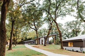 A row of cabins with a pathway leading through a wooded area, string lights overhead, and picnic tables. - Texas Tiny Cabins #1 - Cozy Getaway Near Texoma (Grayson County)
