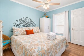 Une chambre à coucher comprenant un lit, un ventilateur de plafond, une armoire et une fenêtre avec des stores.