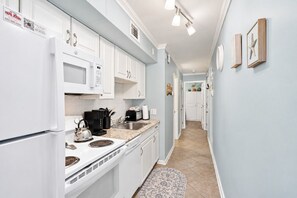 A modern kitchen with white cabinetry, a microwave, a stove, and a sink. - A Place at the Beach - Windy Hill 308 - 2BR 2BA Condo North Myrtle Beach Pool & Hot tub (North Myrtle Beach)