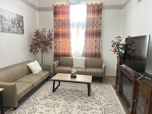 A living room with two sofas, a coffee table, a TV, and a large window with curtains. - Fantastic 5-bedroom family house with AC in vibrant Albuquerque (Albuquerque)