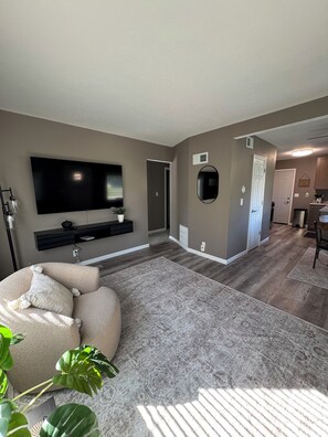 A living room with a flat-screen TV, a large beige sofa, and a patterned rug.